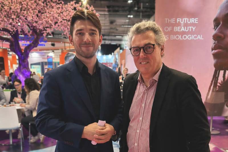 Two men at a beauty trade show, discussing the future of biological skincare.