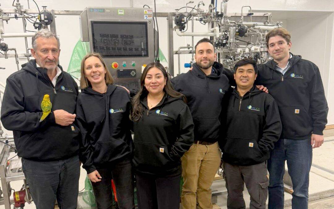 Syklea US team members pose in front of lab equipment, wearing branded hoodies.